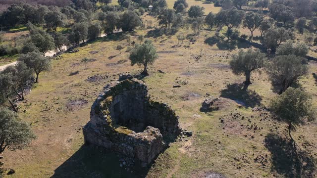 Orbital drone flight to a medieval ruined hermitage from the 11th century as a central point surrounded by pastures oaks and olive trees next to a rural road in the Tietar Valley, Avila Spain