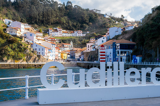 Colorful rural village Cudillero sunny coastal scenery with vibrant houses, beach, and tourism sign.