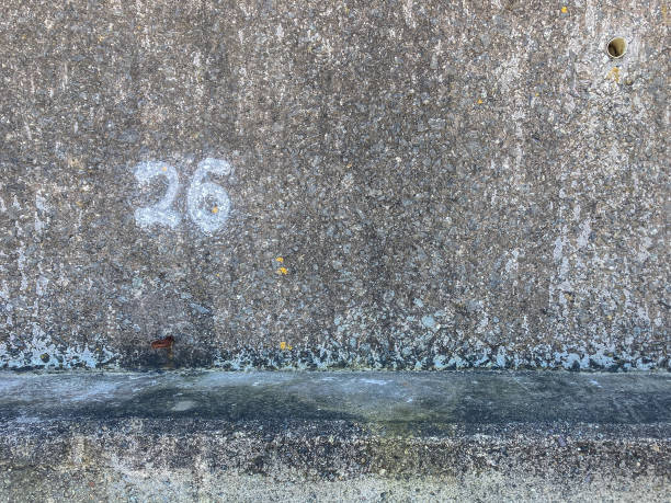 istock Number 26 painted in white paint on to a Beach Concrete protective wall - to show here an allocated beach hut is to be located 2149169521