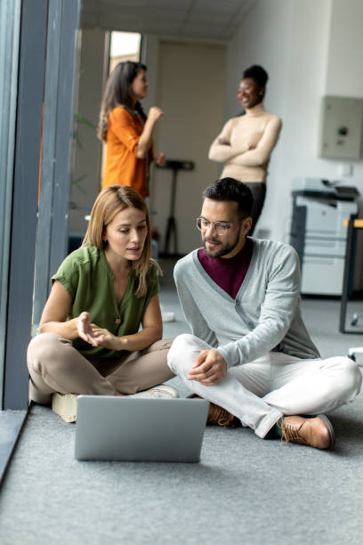 istock Business colleagues sitting on the ground and working on a laptop inside modern office 2149170039