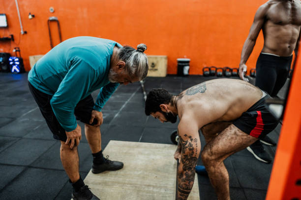 istock Fitness instructor helping student with weightlifting at gym 2149170088