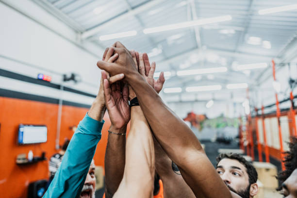 Low angle shot of a group of sports team forming a huddle with their hands. Sports team stacking hands together before the game. Sky with clouds in the background