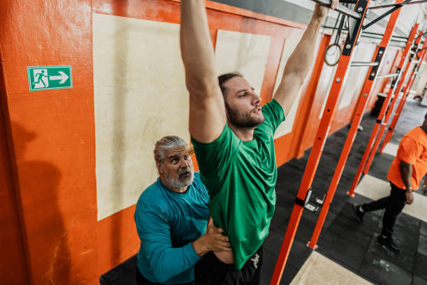 istock Fitness instructor helping student with chin-ups at gym 2149170329