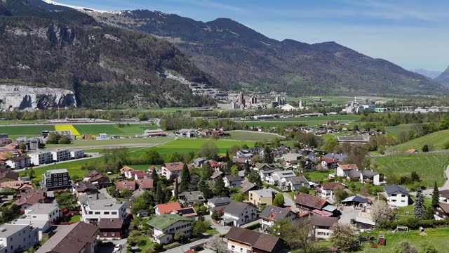 Establishing drone shot over swiss town with modern solar panels on roof of houses. Idyllic landscape with green mountains and fields in spring. Aerial forward shot.