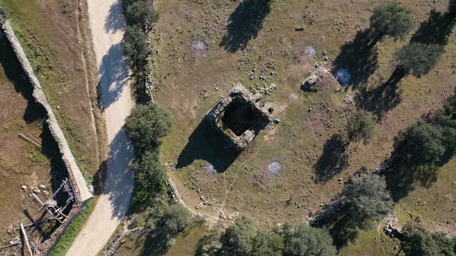 Ascending and orbital drone flight to a hermitage in medieval ruins from the 11th century surrounded by remains of stone walls pastures oak trees next to a rural road in the Tietar Valley, Avila Spain