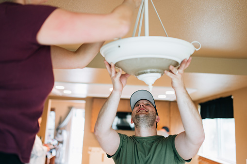 A Caucasian couple install a light fixture in the interior of their house for a  renovation project.