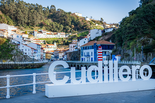 Photograph captures Cudillero's rural charm, vibrant houses, beach, Cudillero sign, sunny day.