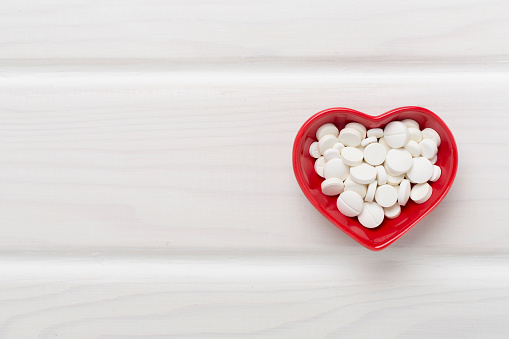 Medicines in heart-shaped bowl on wooden background, top view