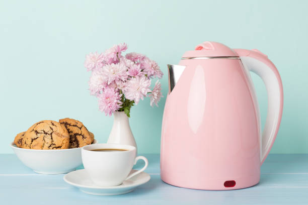 Pink electric kettle with cup of tea and dessert on table