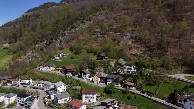 Aerial approaching shot of suburb neighborhood of Trimmis, small town in Switzerland. Mountain road to summit between forest trees in spring. Swiss apartment hotels in city.