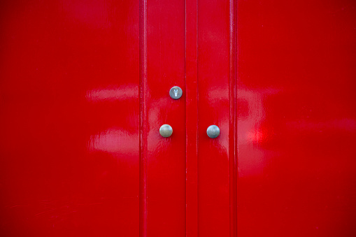 Close-up on a red door with two silver doorknobs and keyhole.