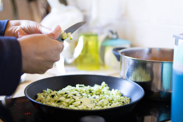 side view of the hands of an unrecognizable woman cutting vegetables for frying in the frying pan on the ceramic glass stove. vegetable food consumption and healthy eating.
