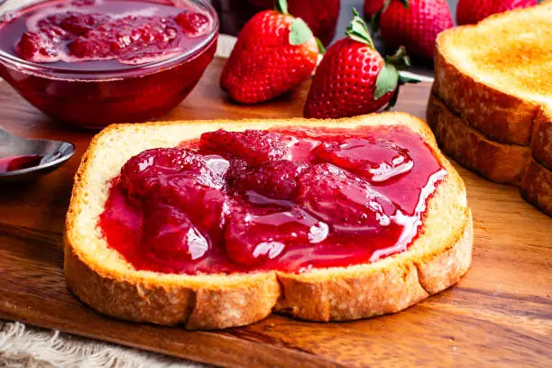 Sliced and toasted white bread and homemade strawberry preserves with large slices of fruit
