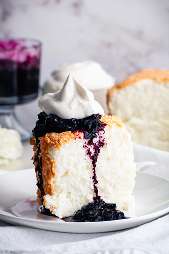 Slice of sponge cake topped with dripping blueberry jam and chantilly cream on a plate