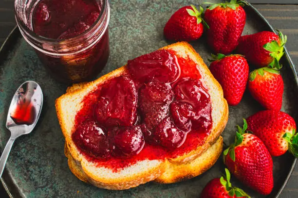 Sliced and toasted white bread and homemade strawberry preserves with large slices of fruit