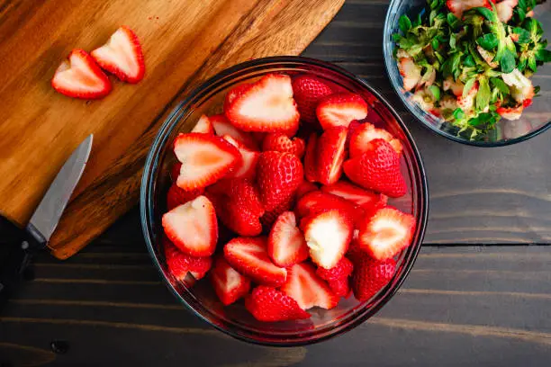Big bowl of fresh, ripe strawberries with their stems and leaves removed and sliced in half