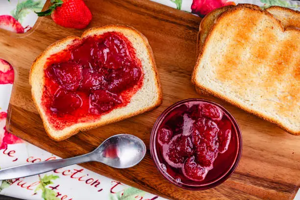 Sliced and toasted white bread and homemade strawberry preserves with large pieces of fruit