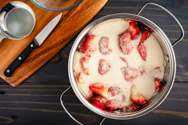 Halved and sliced ripe strawberries covered in organic cane sugar in a saucepan to macerate