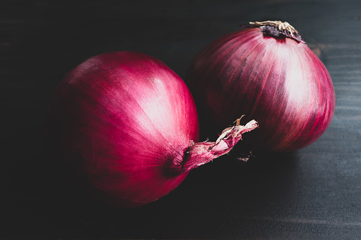 Vintage-style photo of a group of two purple Spanish onions on a dark wooden table