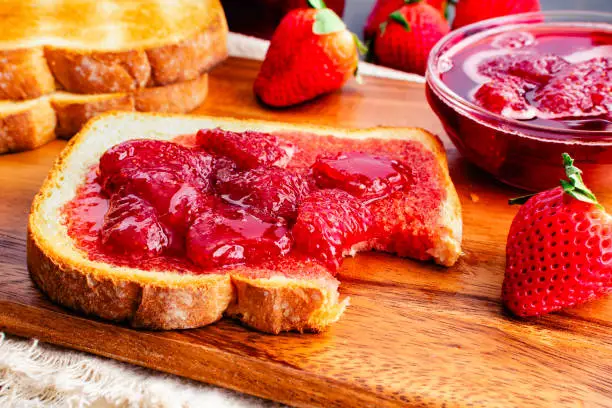Bitten piece of toasted white bread covered with homemade strawberry preserves