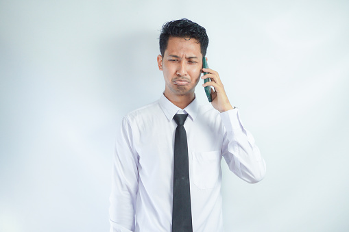 Adult Asian man showing stress expression when answering a phone call