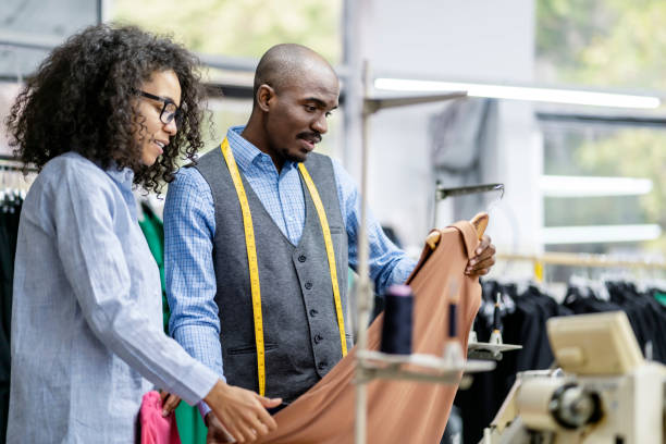 istock African - american young colleagues having discussion at a clothes manufacturing studio, the woman sewing at a modern sewing machine 2149181080