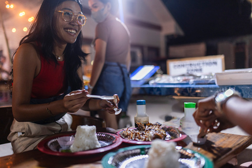 Two Filipino lesbian women eat fish in an outdoor local food bar