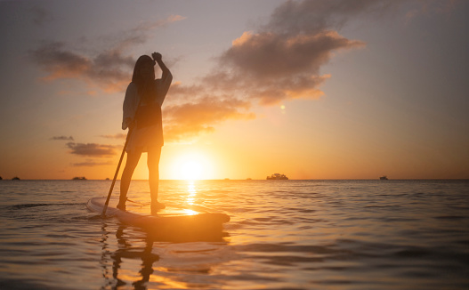 A female tourist enjoys stand-up paddle boarding during a magnificent sunset