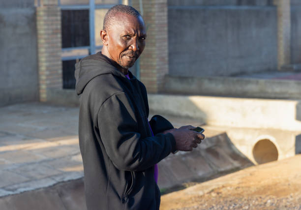 mid adult african man casual dressed with a black hoodie using the phone , outdoors in the neighborhood in a sunny day at sunset