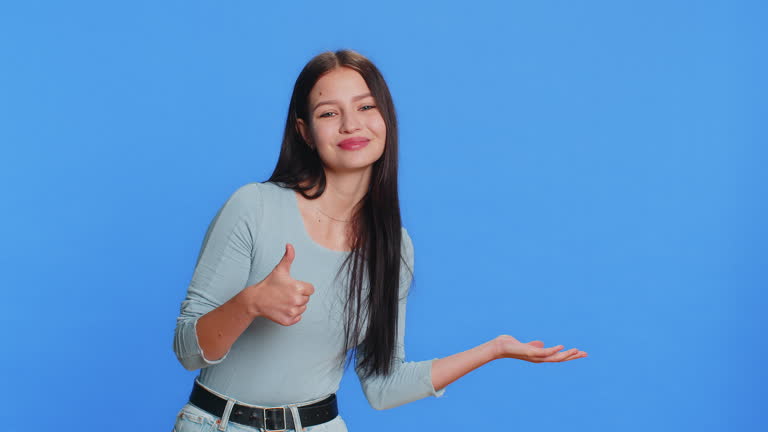 Young woman showing thumbs up and pointing at right on blank space place for your advertisement logo
