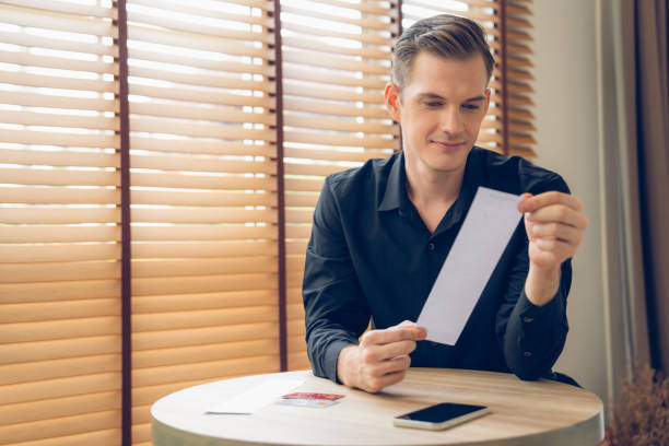 istock Happy man sit at table, smiling as he pays bills with credit card. Unveiling 2149185845