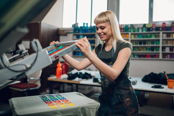 istock Smiling print shop worker silkscreen printing on t-shirt at facility. 2149186065