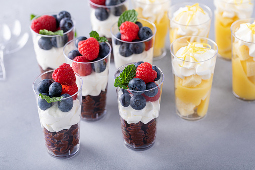Variety of mini desserts in cups, lemon and chocolate desserts with whipped cream and berries served for a party