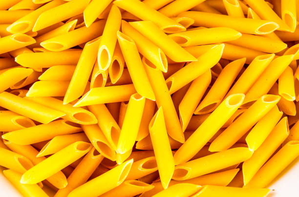 A pile of yellow pasta with a white plate underneath. The pasta is long and thin, and it looks like it's been cut into small pieces