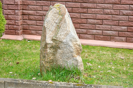 A large stone lies on the grass in front of a red brick fence