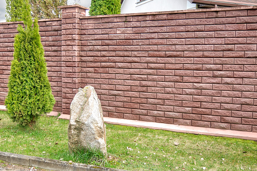 A red brick fence in front of the house next to a stone and a thuja tree