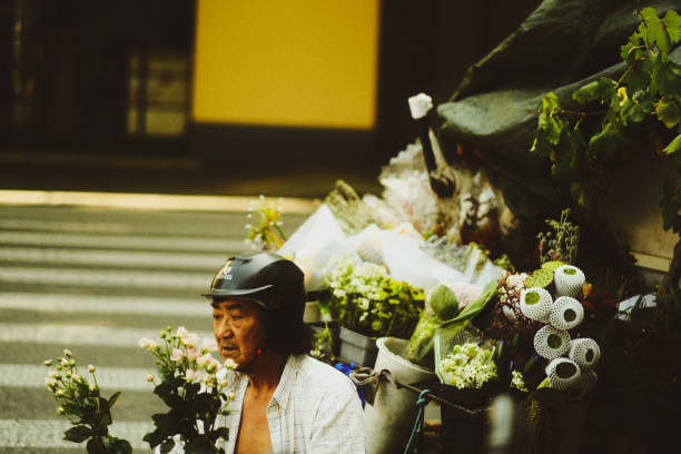 An older man with a helmet driving a motorized three wheeled vehicle filled with flowers for sale