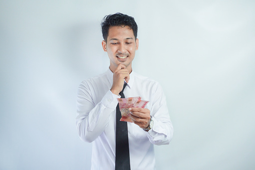 Adult Asian man doing thinking gesture while holding Indonesia paper money