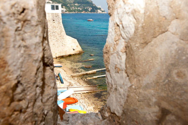 Small colourful dinghies on beach through gap in rock cliff. at Dubrovnik in Croatia.