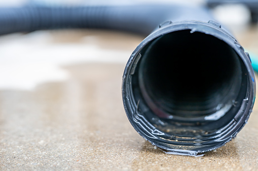 Selective focus on the front opening of a residential sump pump discharging water from the end of a flexible black hose. High quality photo