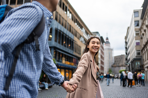 Asian young man and woman shopping goods outdoors in department store. Attractive couple hold shopping bags then walking together with happiness, enjoy purchasing in shopping mall marketplace center.