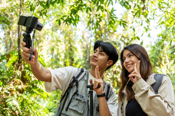 istock Asian two young backpacker vlogger have fun travel in forest together. Attractive man and woman friend traveler use camera record video vlog and walking in nature wood with happiness during holiday. 2149197895