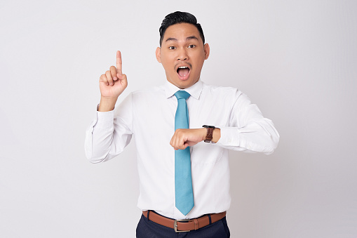 Excited young Asian businessman wearing a formal shirt tie watch looking at the camera while pointing finger up, having great idea, got solution to his problem isolated on white background