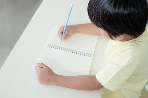 High angle view of a boy writing and doing his homework at home