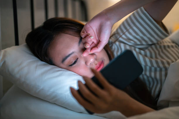 istock Exhausted Asian young woman hurt eye while using mobile phone at night. Attractive girl lying down on bed, feeling tired visual eye strain from watching movie and massage dry irritable eye at home. 2149199690