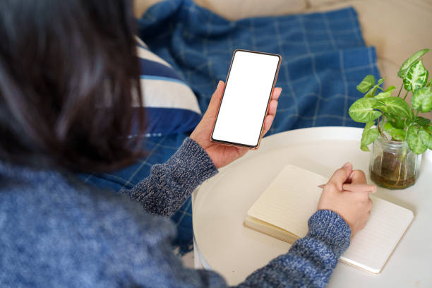 istock In the cropped image, an Asian woman is sitting relaxed on the sofa, using a blank screen smartphone. 2149201460