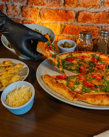 A gloved hand serving a fresh veggie pizza slice on a wooden table