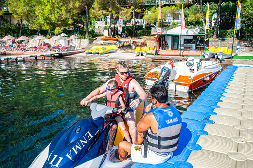 Marmaris, Turkey - September 14 2015: Father and son wearing life jackets are getting ready ride jet ski and talking to the instructor before they go