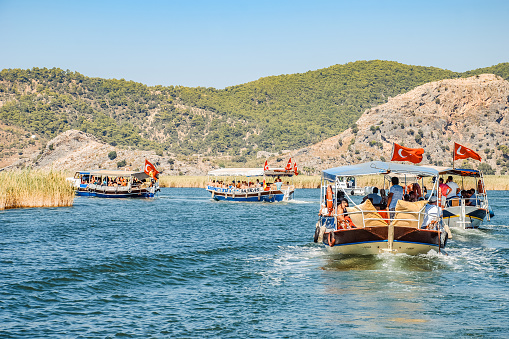 Dalyan, Turkey - September 13 2015: Tourist boats with passengers under canopies navigating river surrounded by tall reed with mountains in background