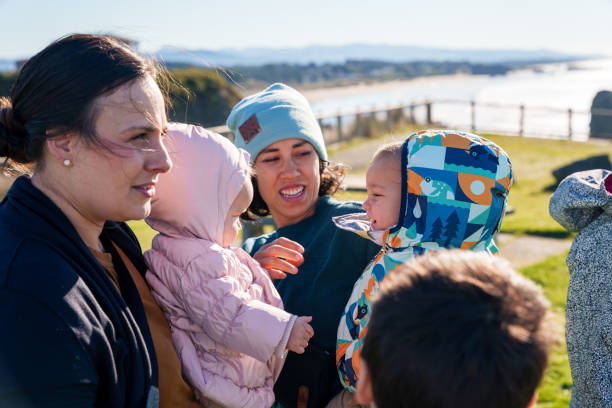 Two cute multiracial babies who are cousins playfully interact while being held by their mothers. The family is enjoying time outside in Bandon, Oregon while on a winter vacation together.